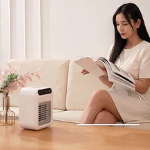 Woman reading a magazine next to a small white mini air cooler in a living room.